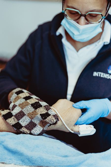 Eine Pflegekraft mit Handschuhen misst die Vitalzeichen eines Patienten mit einem Monitor im Rahmen der Ambulanzpflege.