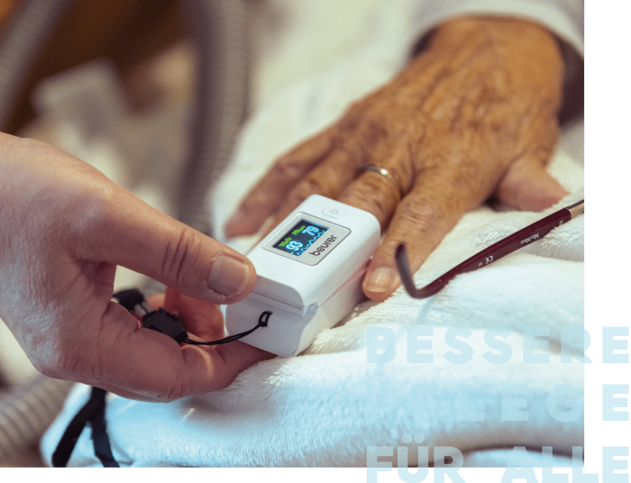 Eine Hand überprüft mit einem Pulsoximeter die Vitalzeichen einer anderen Hand auf einer weißen Decke.