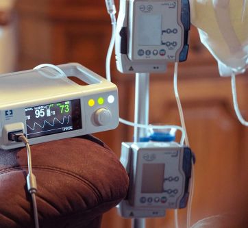 Ein medizinisches Gerät zur Überwachung von Vitalzeichen steht neben Infusionspumpen in einer häuslichen Intensivpflege-Umgebung.