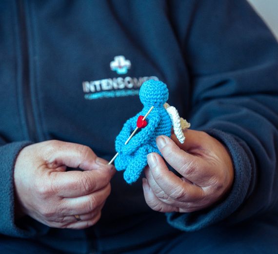 Eine Person hält eine gehäkelte Figur in blauer Farbe mit einem roten Herzen.