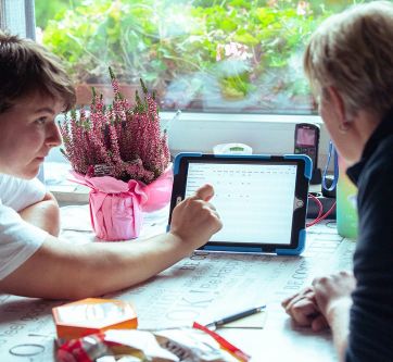 Zwei Personen sitzen an einem Tisch und besprechen gemeinsam Informationen auf einem Tablet.