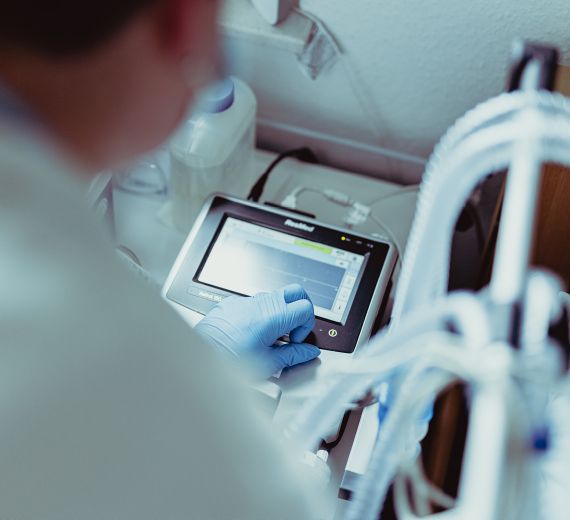 Eine Person bedient ein medizinisches Gerät mit Touchscreen zur Überwachung von Patientendaten in einem klinischen Umfeld.