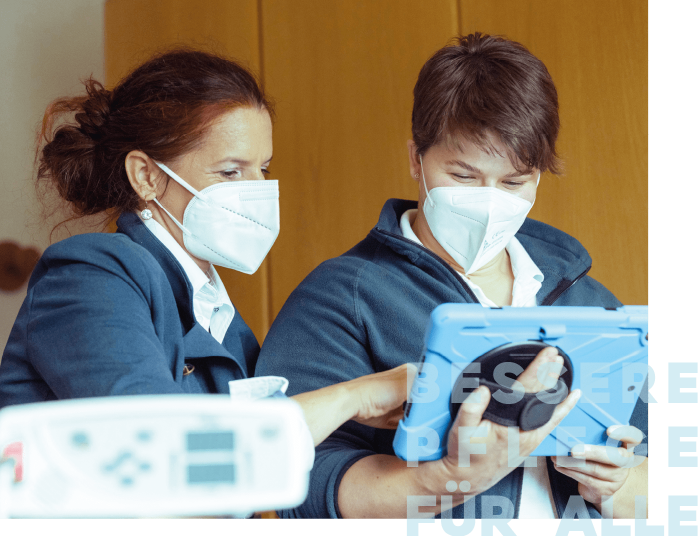 Zwei Frauen in Masken betrachten gemeinsam ein Tablet.