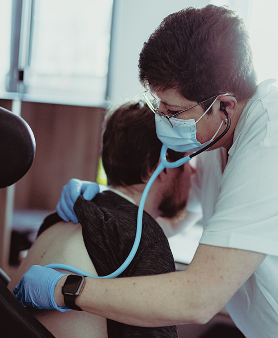 Ein Pflegekraft hört mit einem Stethoskop die Lunge eines Patienten bei der Intensivpflege zu Hause ab.
