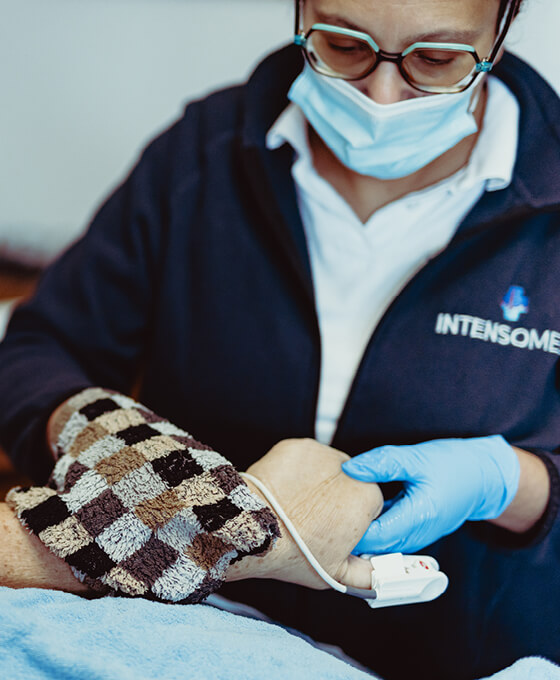 Eine Pflegekraft mit Handschuhen und Maske überwacht die Vitalzeichen eines Patienten mit einem Monitor in der ambulanten Pflege.